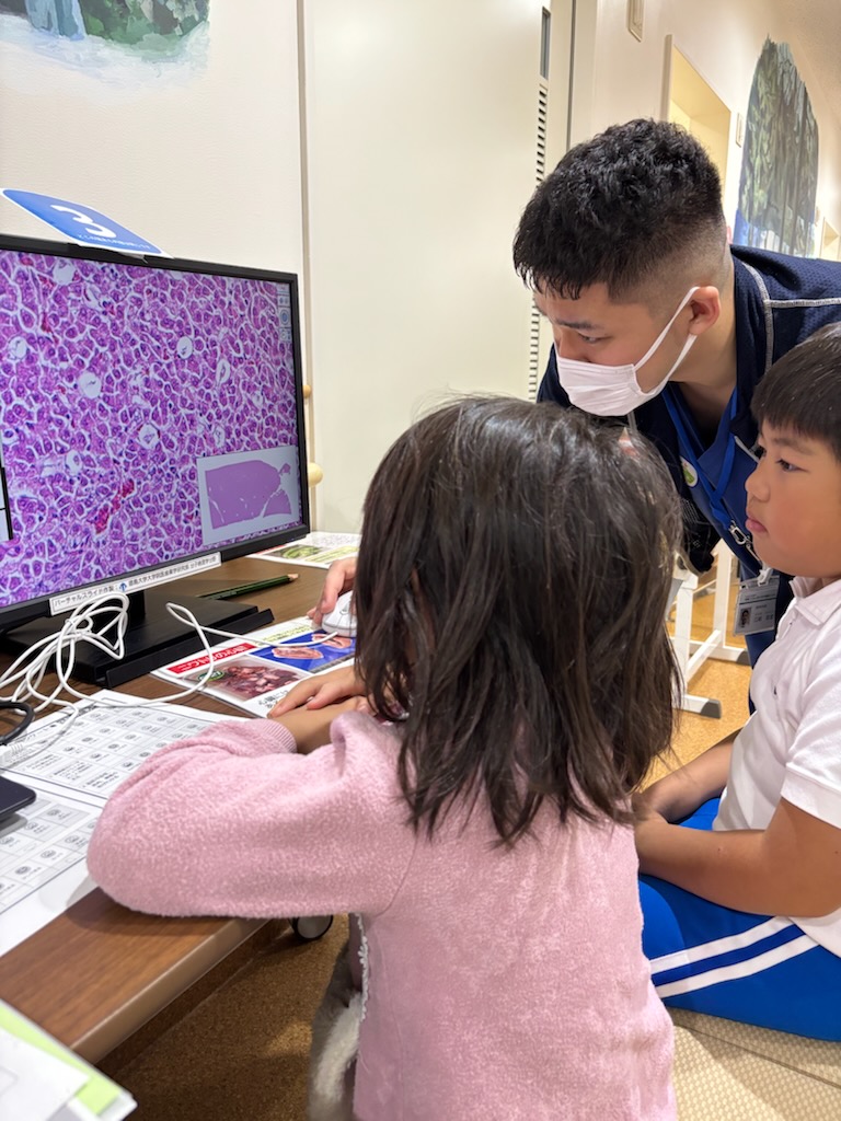 病院フェスティバルでデジタル病理画像を使った観察体験を案内する研修医と参加する子どもたち